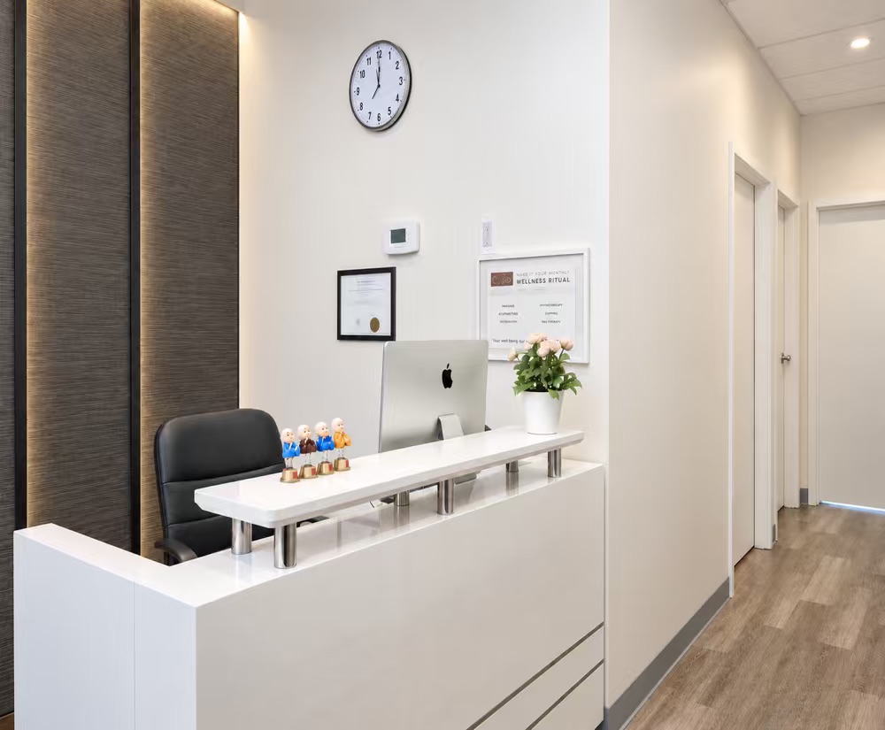 White reception desk with a computer and flowers beside the clinic hallway